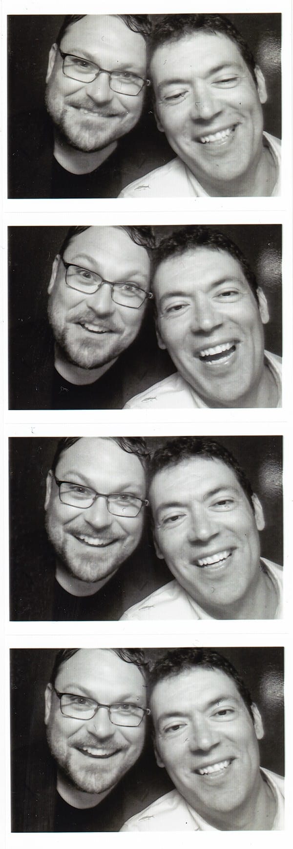 A black-and-white photo booth strip of David Zeltser and Benjamin Arthur, cheek to cheek and grinning, four frames from top to bottom.